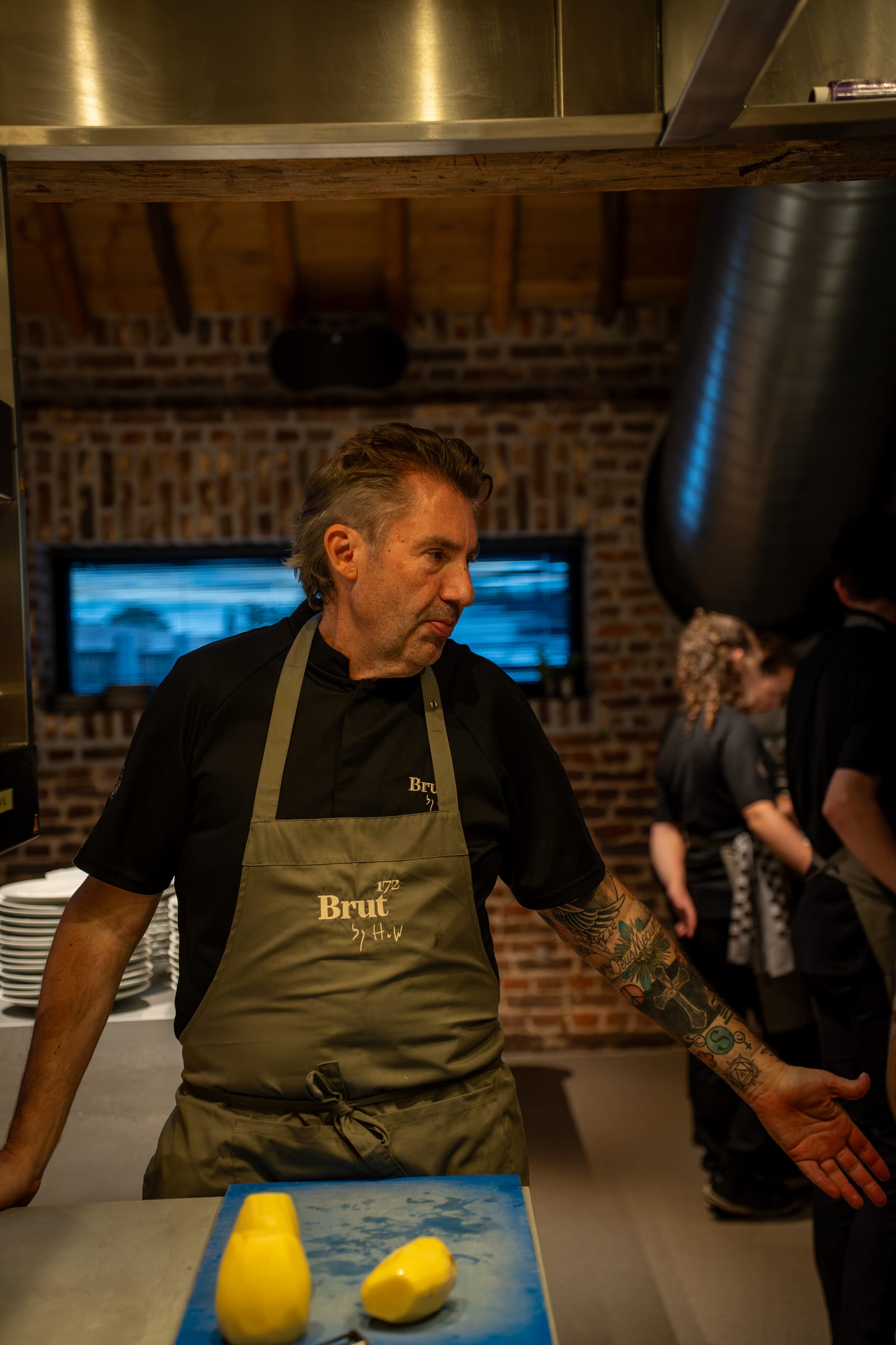 Hans van Wolde in de keuken in een groen schort van Brut172, met twee geschilde knollen op een snijplank voor hem